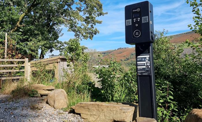 an electric vehicle charger standing by rocks and surrounded by shrubs and trees with blue sky